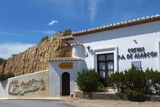 White building with restaurant and painted rock face, surrounded by shrubs and a sunny sky, Pedro