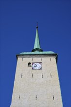 Historic church tower with green copper spire and built-in clock in front of a clear blue sky,