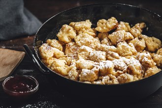 Kaiserschmarrn in a pan sprinkled with sugar, jam, dark background