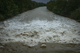 A powerful river with a strong current under a cloudy sky, surrounded by green trees, Schwarza,