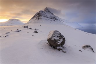 Stones lying in the snow in front of a pointed mountain, snow, winter, cloudy mood, fjord, Sudavik,