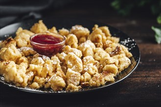 Kaiserschmarrn on a black plate with icing sugar, small bowl with red jam, dark background