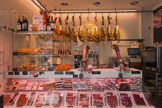 Modern butcher's shop with meat counter, hanging hams, sausages and wine bottles on display,