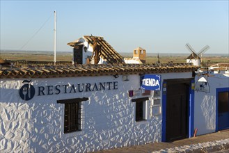 Rustic building with restaurant sign and white-blue walls, windmills in the background under a