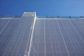 Shielding of a building by a tarpaulin attached to scaffolding against a clear blue sky, Bergen,