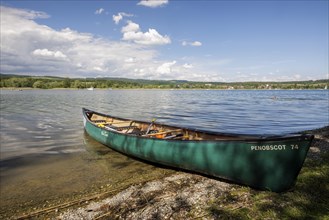 Green canoe on the shore of a lake with clear water and cloudy sky, quiet peaceful surroundings,