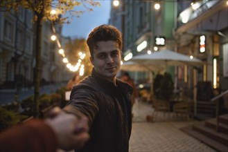 Follow me. Beautiful romantic man takes his girlfriend hand while walking in the evening city