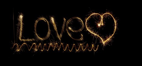 Inscription Love and heart of sparklers. Sparks of holiday lights on black background with heart