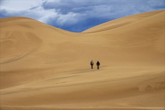 Two travelers in the desert. Hiking on sand dunes in mountains. Gobi desert, Mongolia, Asia