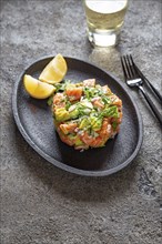 PERUVIAN NIKKEI FOOD. Salmon avocado ceviche on black plate, black background top view