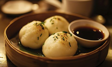 Three white dumplings with parsley on top sit in a bamboo basket. A small bowl of sauce is placed