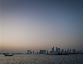 Doha city skyscrapers urban skyline view and dhow boat in qatar at sunset