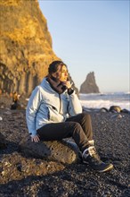 Portrait of a woman sitting on the black sand beach of Reynisfjara looking at the sea. Iceland