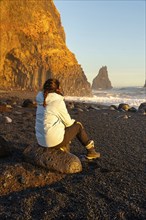 Woman on the black sand beach of Reynisfjara sitting looking at the sea. Iceland