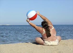 Overweight woman doing gymnastics with ball on beach