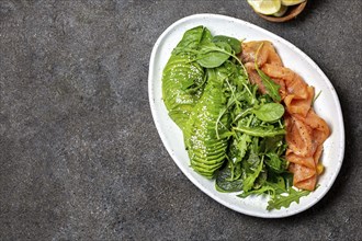 Low carbs salad. Spinach, rucola salad with avocado and salmon. Black concrete background, top view