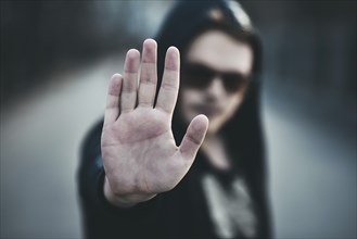 Portrait of fashion man in a black sweater with a hood and sunglasses, hand gestures