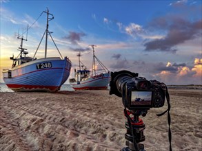 Tripod with camera in front of fishing boats on the beach in Vorupor, Denmark, Europe