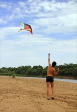 Asian boy running kite on river beach