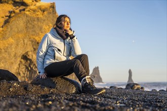 Portrait of pretty woman sitting on the black sand beach of Reynisfjara by the sea. Iceland