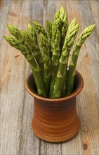 A bunch of asparagus in a ceramic pot on a wooden background