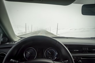 Car interior point of view on road cleared from snow and ice, but piled up on the side of the road.