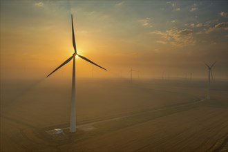 Beautiful aerial sunset landscape with windmills or wind turbine on wind farm in rotation to