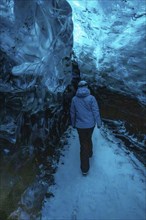 A woman is walking through a blue cave. The cave is illuminated by blue light, creating a serene