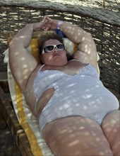 Vacation, overweight woman lying on beach