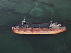 Top view of an old tanker that ran aground, overturned and polluted the coast with oil spilled from