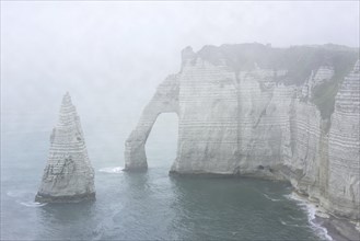 L'Aiguille and the Porte D'Aval, a natural arch in the chalk cliffs at Etretat in the mist, Côte