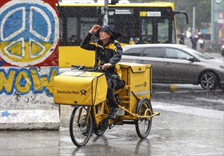 A DHL mail carrier rides his e-bike along a pavement in heavy rain, Berlin, 23 06 2023