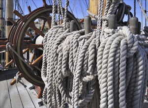 Steering wheel and ropes coiled around belaying pins aboard the Grand Turk, Etoile du Roy, a