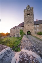 Entrance to the medieval castle with cobbled path and warm sunset in the background, Harz