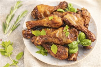 Smoked chicken legs with herbs and spices on a ceramic plate with linen textile on a brown concrete