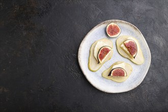 Summer appetizer with pear, cottage cheese, figs and honey on ceramic plate on a black concrete