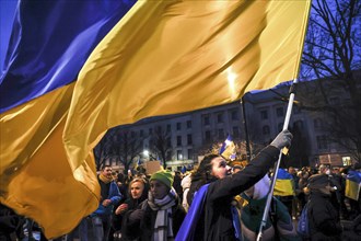 A woman with a large Ukrainian flag demonstrates in front of the Russian embassy on the anniversary