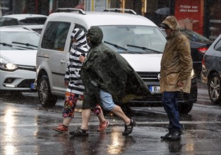 People in rain gear walking across a street in heavy rainfall, Berlin, 23 06 2023