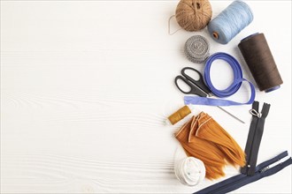 Sewing accessories: scissors, thread, thimbles, braid on white wooden background. Top view, flat