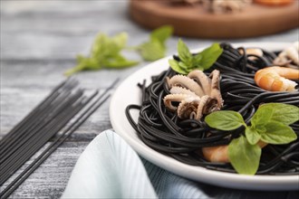 Black cuttlefish ink pasta with shrimps or prawns and small octopuses on gray wooden background and