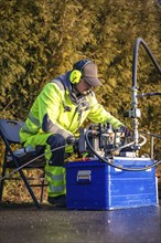 Worker in high-visibility clothing operating a complex outdoor machine, fibreglass construction,