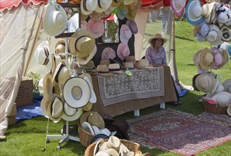 Woman selling hats from tent stall during garden event at Helmingham Hall, Suffolk, England, United