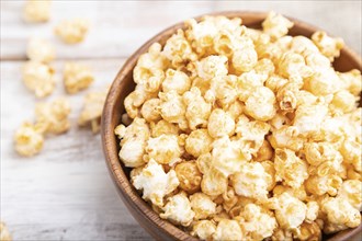 Popcorn with caramel in wooden bowl and a cup of coffee on a white wooden background and linen