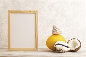 Wooden frame with melon, coconut, seashells on gray concrete background. Side view, copy space.