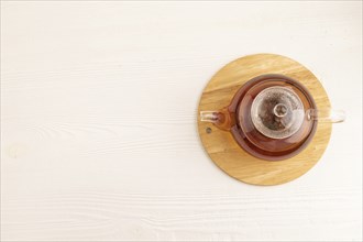 Red tea with herbs in glass teapot on white wooden background. Healthy drink concept. Top view,