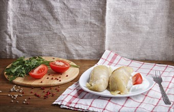 Cabbage rolls with beef, rice and vegetables on a linen tablecloth on a brown wooden background.