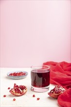 Glass of pomegranate juice on a white and pink background with red textile. Side view, copy space,