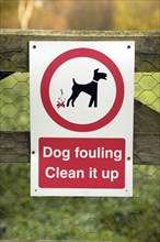 Sign saying Dog fouling Clean it up on fence, UK