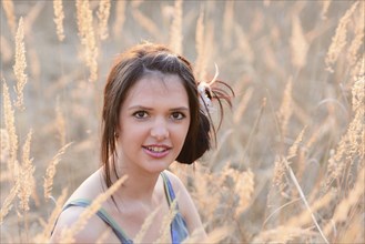 Woman with styled hair sitting among dry reeds, smiling at the camera, Bavaria