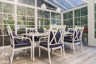 White dining table and armchairs with blue cushions in sunroom at back of luxurious residential